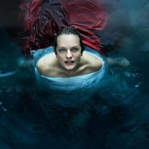 Woman swimming, emerging from water, wrapped in red and white fabric amidst dark, mysterious surroundings.