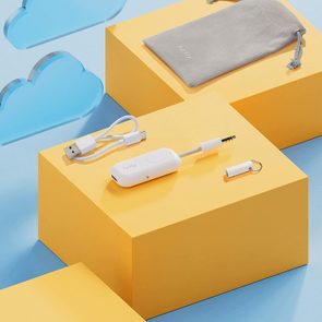 White device lies on yellow block, accompanied by USB cable and gray pouch labeled 