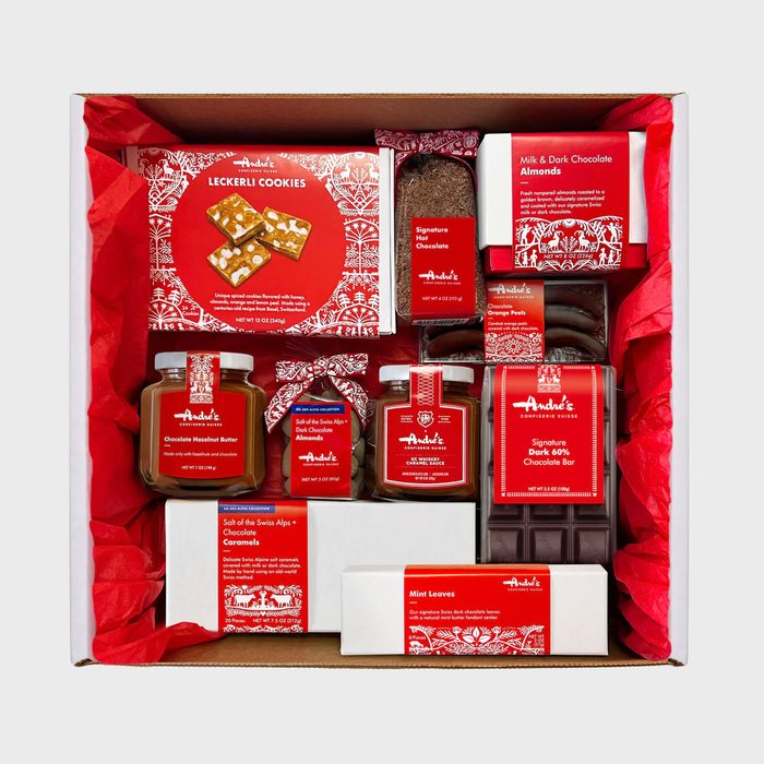 A gift box displays assorted chocolate treats organized neatly, surrounded by red tissue paper. Labels read: 
