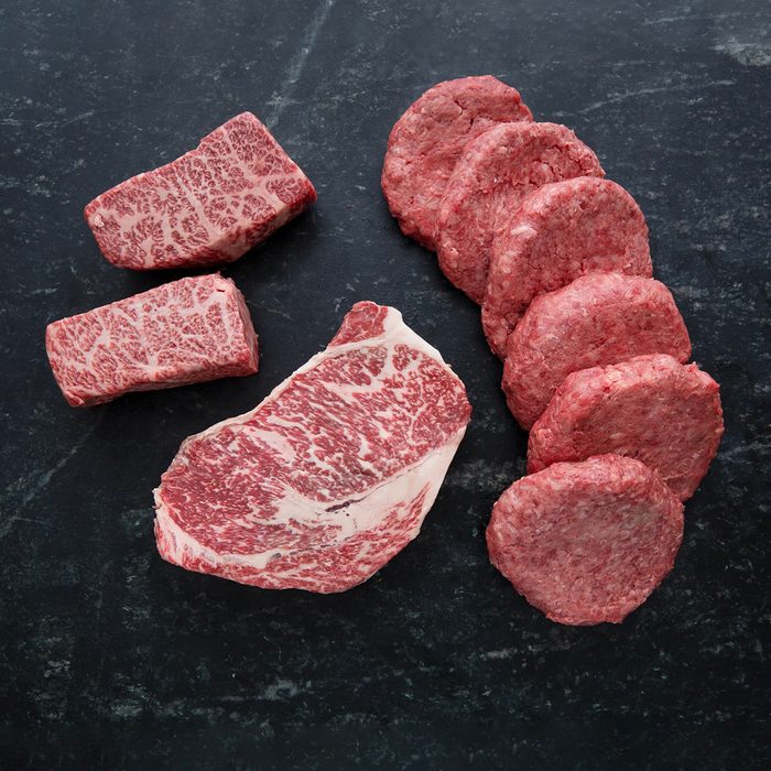 Marbled steak and raw hamburger patties rest on a black slate surface, neatly arranged for display.