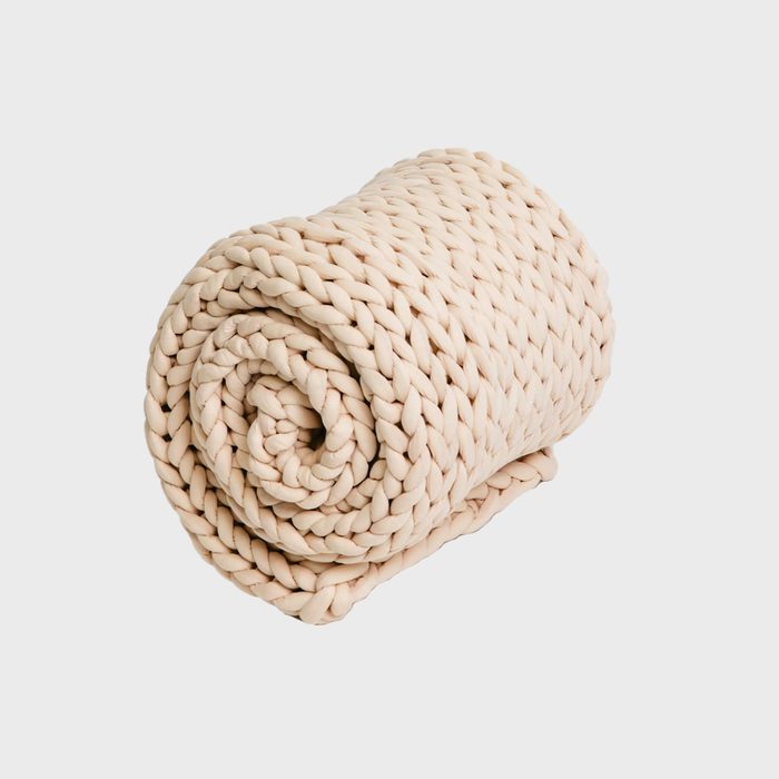 A beige, chunky-knit blanket tightly rolled on a plain, light background.