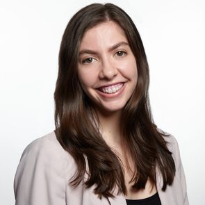 A person smiles warmly, wearing a light-colored blazer against a plain white background.