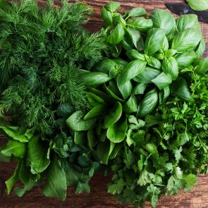 Fresh herbs including basil, dill, and spinach are arranged on a wooden table with a knife nearby.