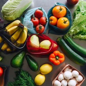 Assorted fruits and vegetables lie together on a table, including bananas, tomatoes, lettuce, and zucchini, creating a colorful, fresh display.