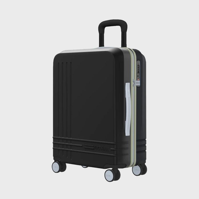 A black suitcase stands upright with extended handle, positioned on four wheels, against a plain light background.