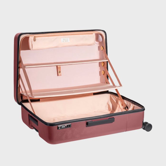 Open suitcase revealing spacious, organized compartments with pink lining and straps, set against a plain gray backdrop.