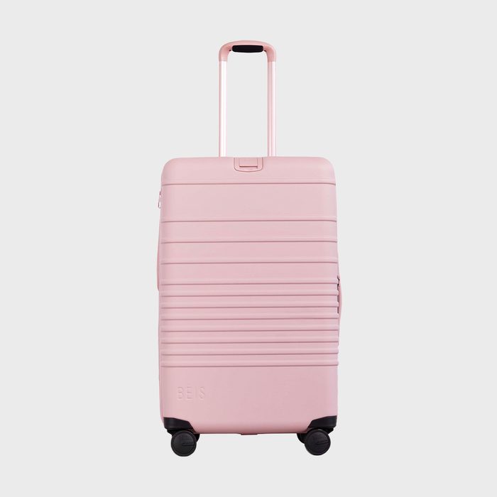 Pink suitcase stands upright; handle extended, resting on four wheels against a plain background. 
