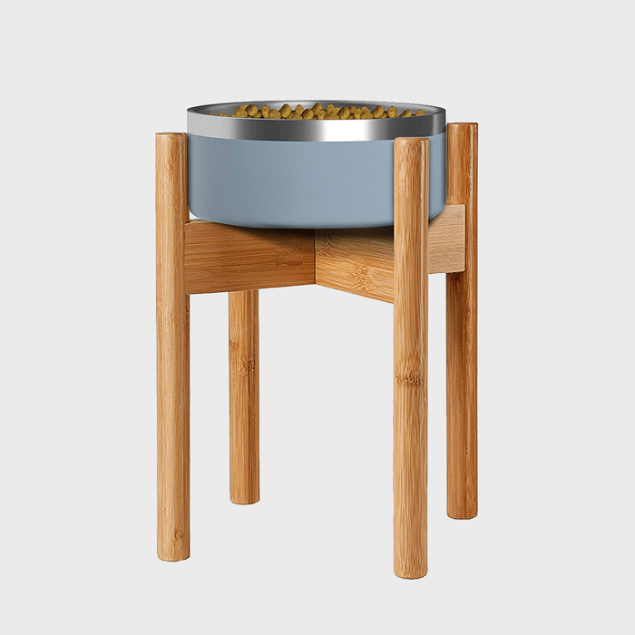 Metal bowl sits on a wooden stand, filled with dry kibble, against a plain, light background.
