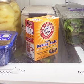Baking soda box sits in a refrigerator surrounded by jars, salad box, and dairy container on a shelf labeled 