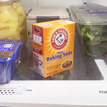 Baking soda box sits in a refrigerator surrounded by jars, salad box, and dairy container on a shelf labeled "Fruit & Vegetable."