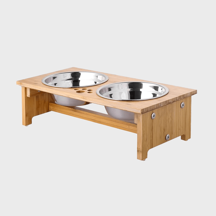 Two stainless steel bowls sit in a wooden stand, designed for pets, against a plain light gray background.