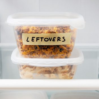 Containers stack in a fridge. Top container labeled "LEFTOVERS" holds rice dish. Bottom container holds diced meat. Shelves are visible.