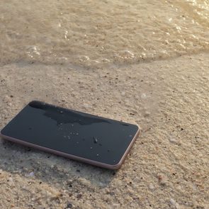 A smartphone lies on wet sand as ocean waves gently approach the shore.