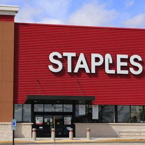Staples storefront features large logo on red facade, situated in a commercial area under a partly cloudy sky.