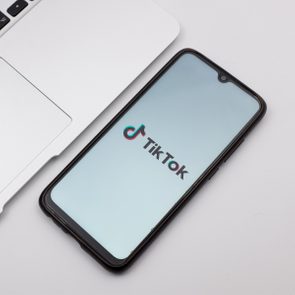 Smartphone displays TikTok logo on screen, lying next to a laptop, on a white surface.