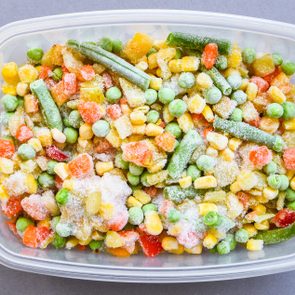 Frozen mixed vegetables sit in a clear plastic container on a gray surface.