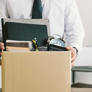 Box holds office items, including books, pencils, an alarm clock, and a calculator, carried by a person in a white shirt and tie.