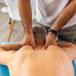 Person receives a shoulder massage on a light blue massage table in a bright room.