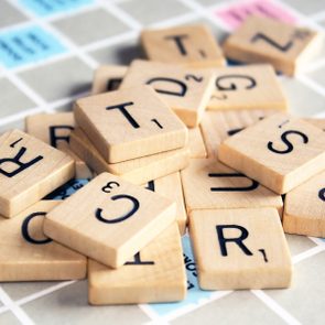 Wooden Scrabble tiles lie scattered on a game board, surrounded by colored squares with point values.