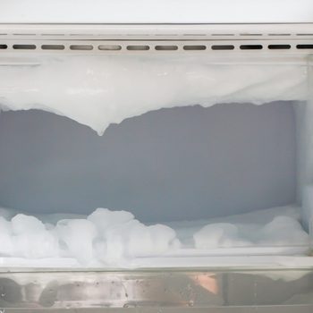 Thick ice accumulation forms inside an open freezer compartment, showing significant frost buildup on the walls and edges.