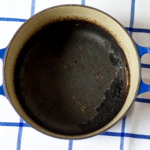 A burnt, empty pot sits on a white and blue checkered cloth.