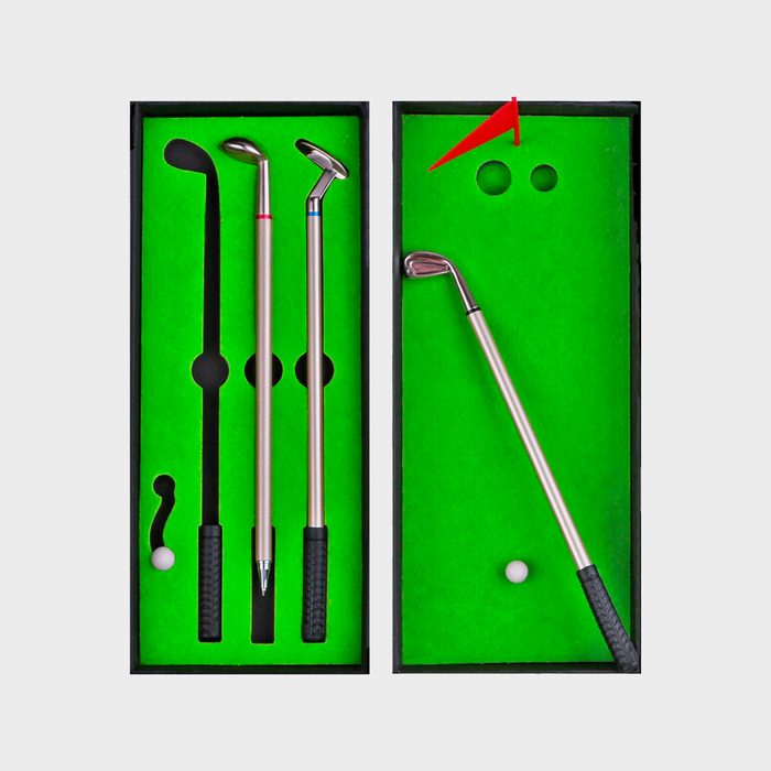 Golf pens sit arranged inside a green box, designed to resemble a mini-golf course with holes and a red flag marker.