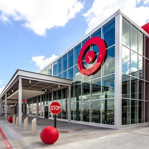 Storefront displays large red logo, stop sign, and entrance canopy under blue sky, with concrete path and red bollards nearby.