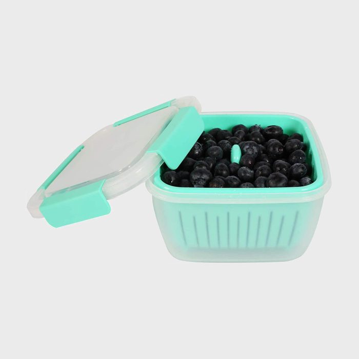 Blueberries sit in an open teal plastic container with a loose lid, set against a plain background.