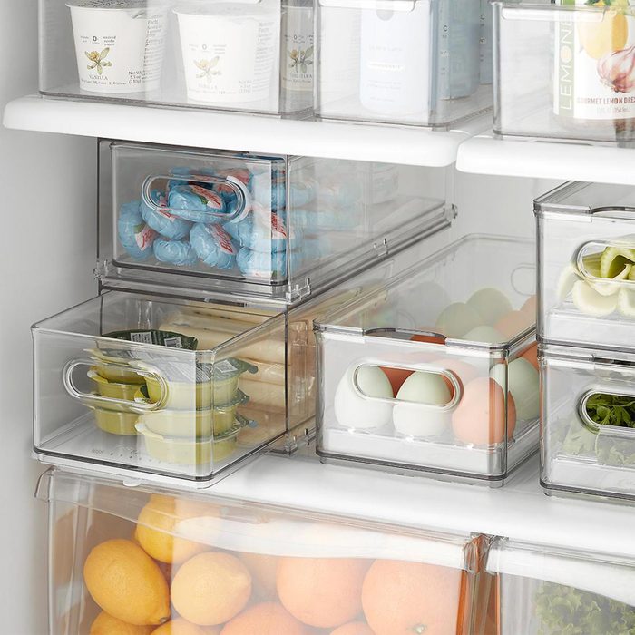 Transparent containers hold various foods like eggs, lemons, and yogurt, neatly organized on refrigerator shelves for efficient storage.