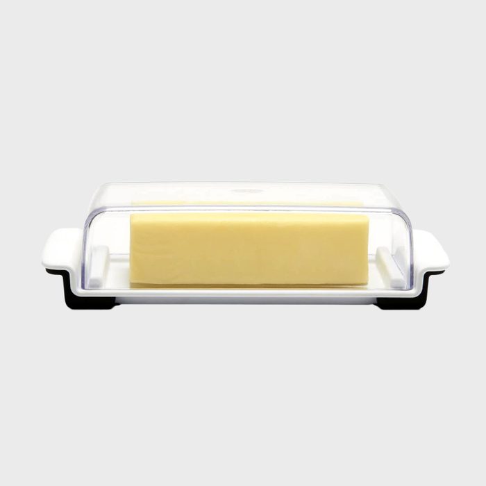 Butter sits encased under a clear plastic lid on a white butter dish against a plain background.