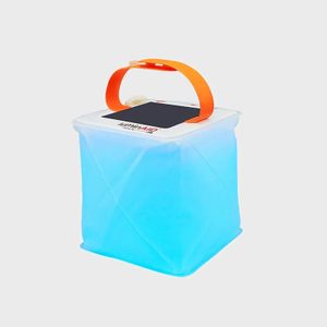 A cube-shaped lantern emits a blue glow, featuring an orange handle and solar panel, set against a plain gray background.