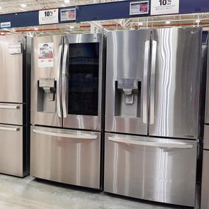 Refrigerators stand displayed in an appliance store, featuring stainless steel finishes and built-in water dispensers, promoting a sale with various discounts.