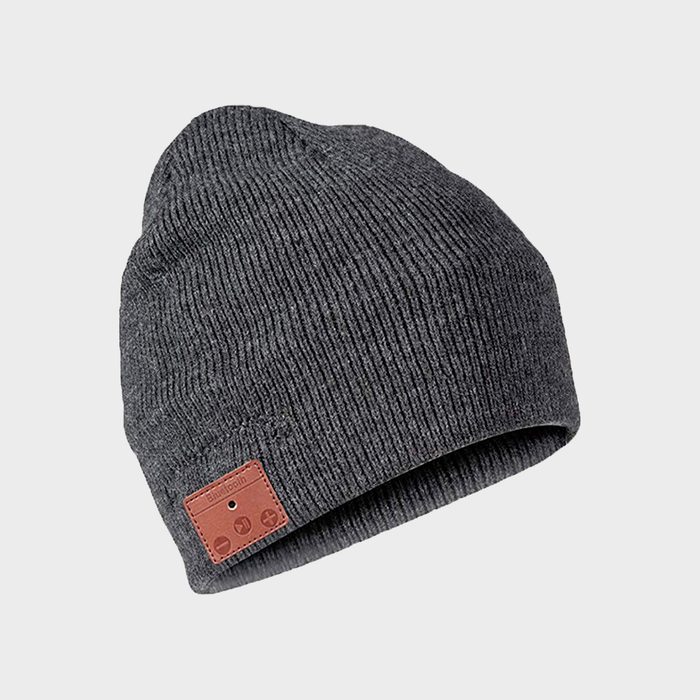 Gray knit beanie tilted against a plain background, featuring a small brown leather Bluetooth control panel on the front.