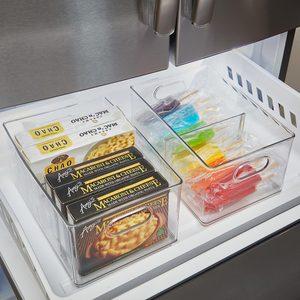Organized freezer drawer holds boxed macaroni and cheese and colorful popsicles in transparent containers, under a metallic refrigerator.