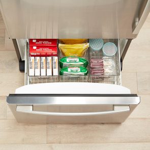 Freezer drawer holds organized packages of food on a kitchen floor; items include mini tacos, veggie spirals, and pineapple chunks.