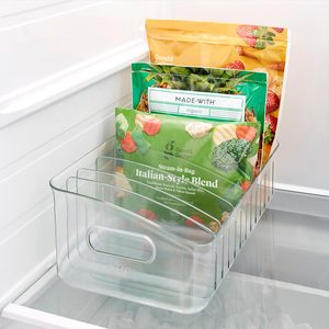 Clear storage bin holds packaged vegetables upright in a refrigerator. Labels include 