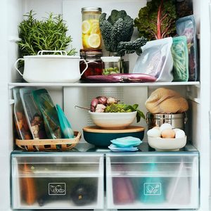Refrigerator holding organized food containers and fresh produce, including jars, leafy greens, and eggs, creating a neat domestic storage scene.