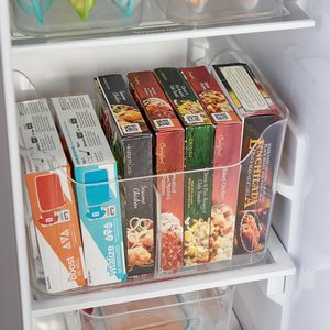 Frozen food boxes are neatly organized in a clear plastic bin inside a refrigerator, surrounded by other stored items.