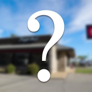 A large question mark overlays a blurred image of a building and street sign under a blue sky.