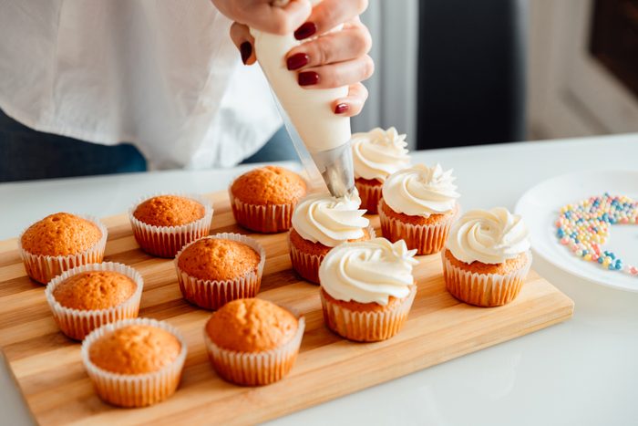 Woman decorates freshly baked cupcakes with cream