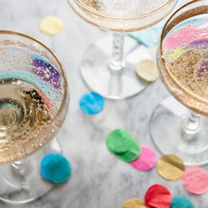 Champagne glasses holding bubbly drinks sit atop a marble surface, surrounded by colorful confetti.