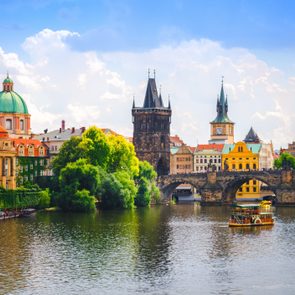 Boat floats on a river beneath a historic stone bridge, surrounded by colorful old buildings and a clear blue sky.