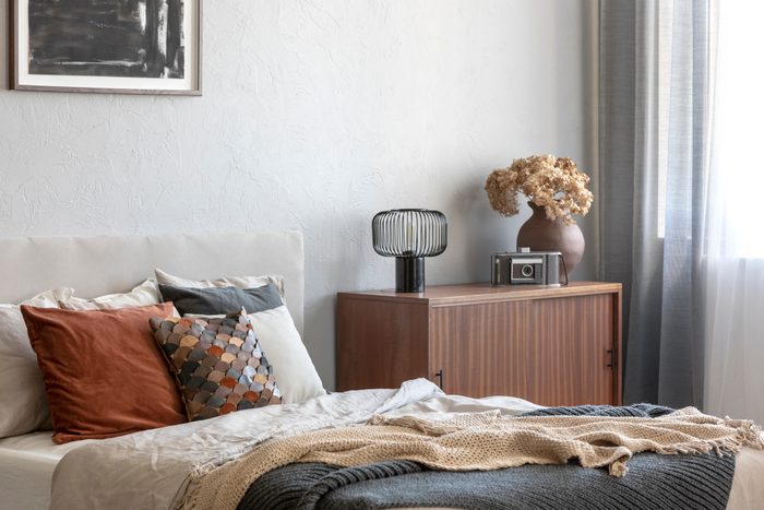 Vintage wooden cupboard next to king size bed with pillows and blanket in trendy bedroom interior