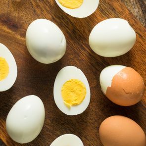 Hard-boiled eggs rest sliced and whole on a wooden board, emphasizing their white exteriors and yellow yolks, with one partially peeled brown egg.