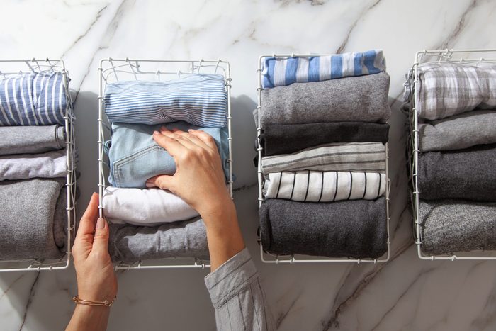 Neatly folded clothes and pyjamas in the metal mesh organizer basket on white marble table