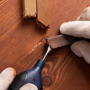 Heating tool melts wax stick, repairing scratched wooden surface.