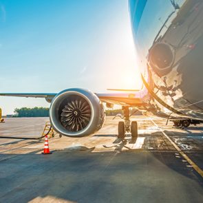 Airplane sits on the tarmac, engine visible, during sunrise; a yellow fuel truck and safety cones are nearby.