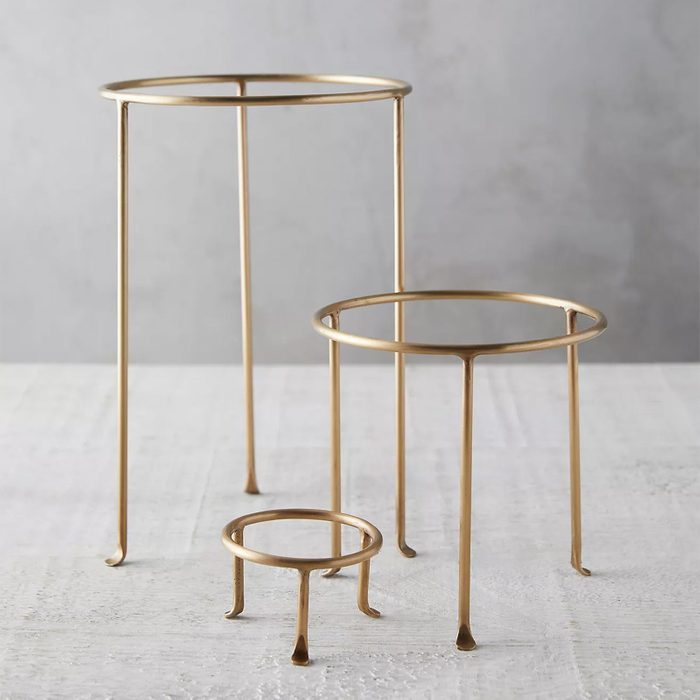 Three gold metal stands of varying heights stand on a white surface with a plain, gray background.