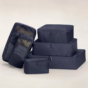 Black packing cubes stacked and arranged on a neutral background, showcasing mesh tops and zippers for travel organization.
