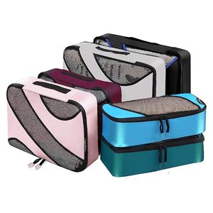 Colored packing cubes arranged in layers; some unzipped showing mesh tops, others stacked. Background is plain white.